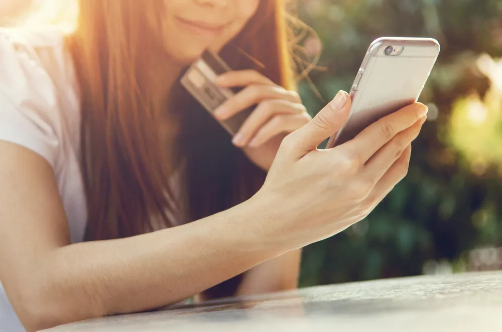 Mädchen, das auf sein Handy schaut und eine Kreditkarte in der Hand hält