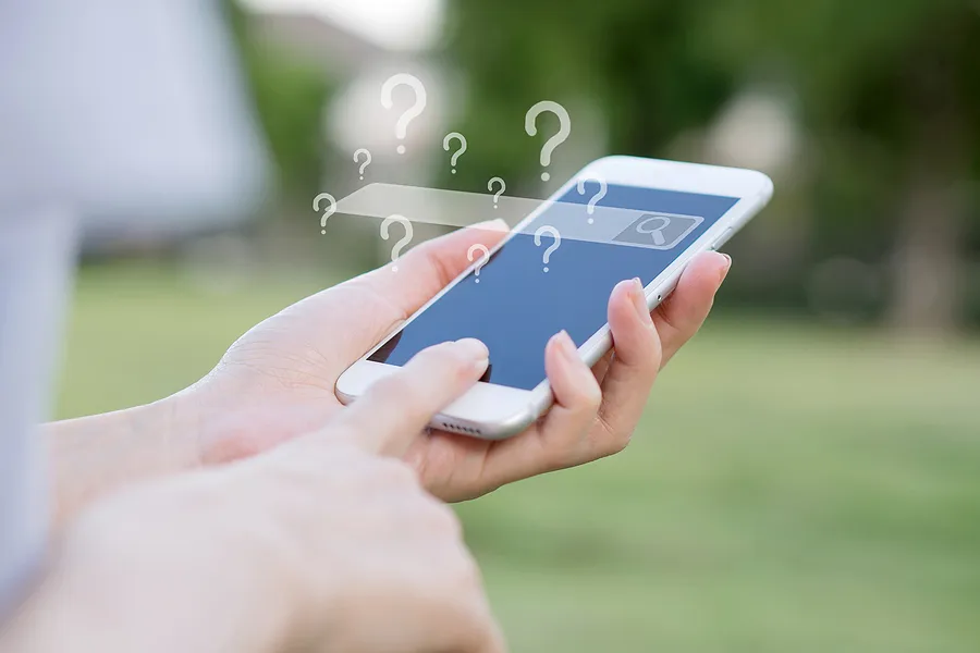 Hände, die ein Smartphone mit einer leeren Suchleiste und vielen Fragezeichen halten