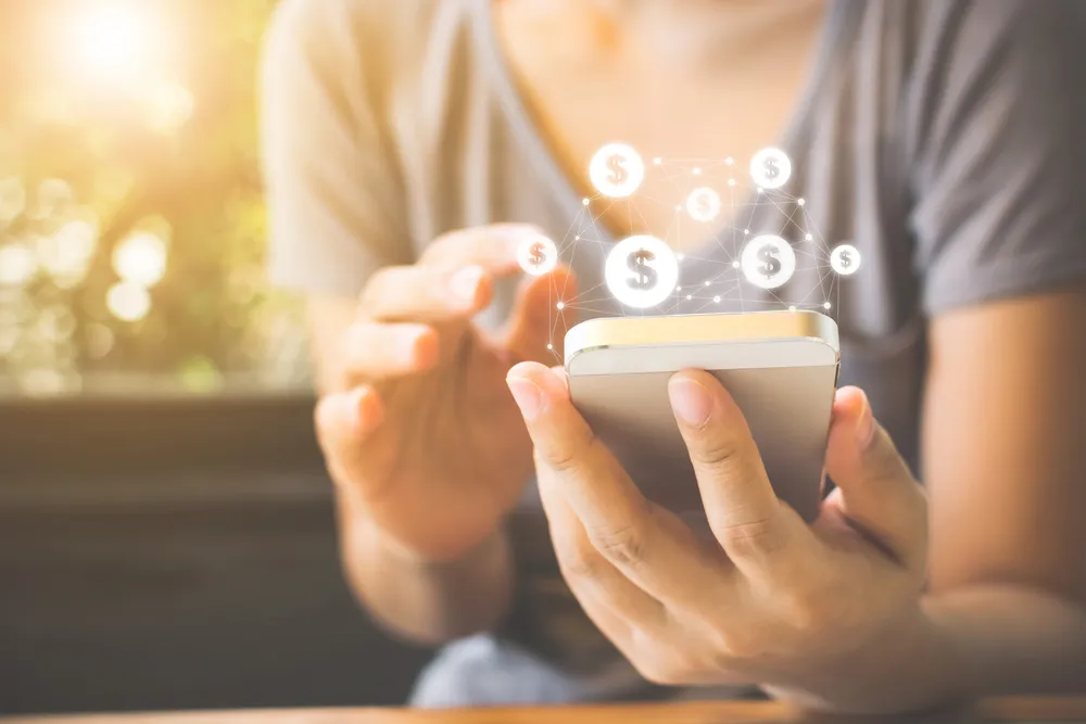 Der Oberkörper einer Person, die ein Handy in der Hand hält, umgeben von Dollarzeichen