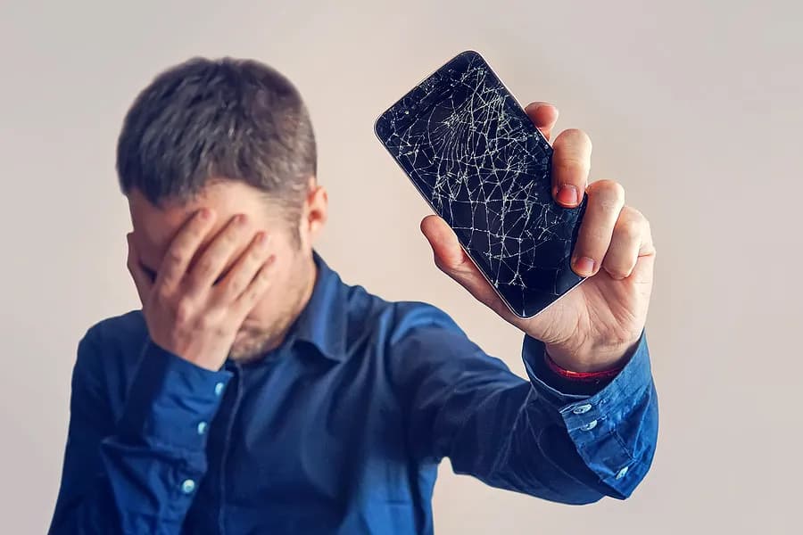 Ein Mann, der sich die Augen zuhält und ein Handy von sich weghält.