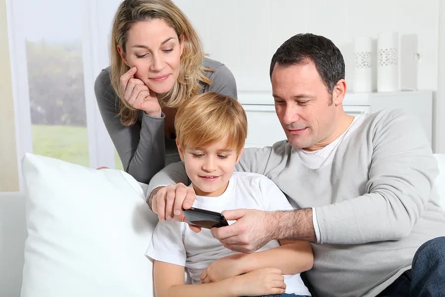 Mutter, Vater und Kind, die auf ein Handy schauen.