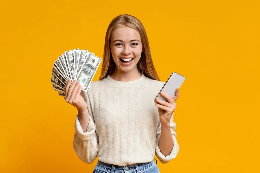 Frau, die ein Handy und Geld in der Hand hält.