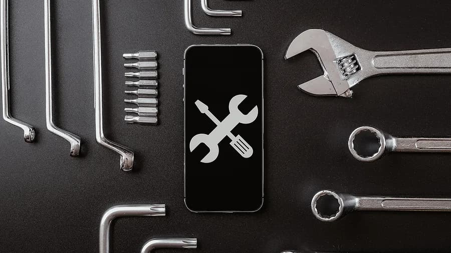 Diagnosewerkzeuge und Konzept zur Smartphone-Reparatur mit einem Handybildschirm, auf dem ein Schraubenschlüssel- und ein Schraubendreher-Symbol zu sehen sind, umgeben von Metallwerkzeugen.