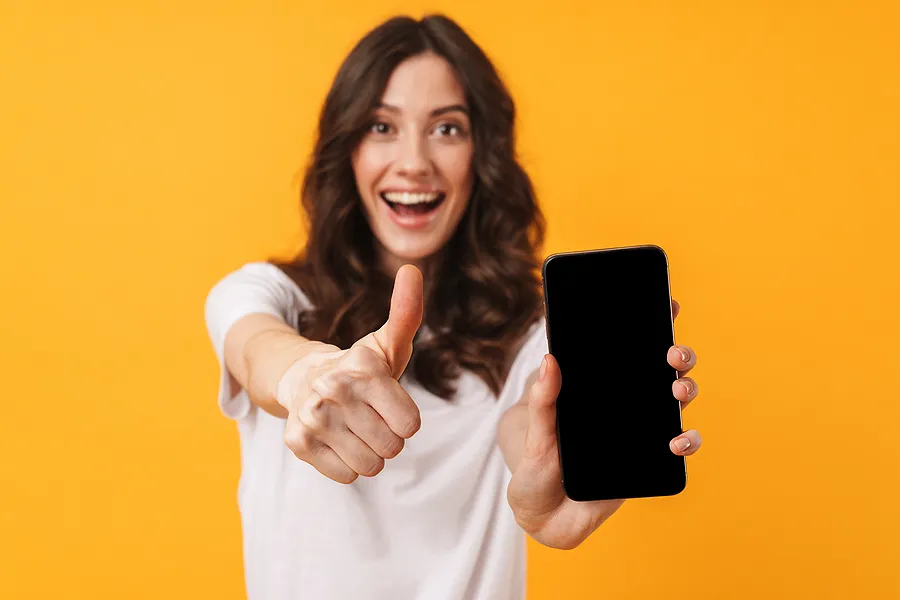 Lächelnde Frau, die ein Smartphone in der Hand hält und den Daumen hochhält – als Symbol für den erfolgreichen Abschluss des Telefonverifizierungs- und Zertifizierungsprozesses.