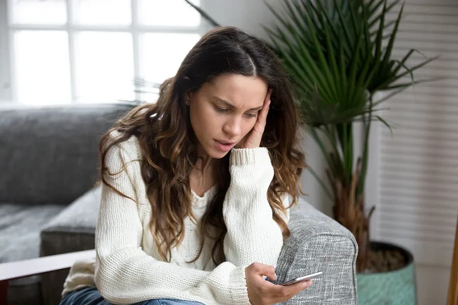 Eine besorgte Frau, die auf ihr Smartphone schaut – dies verdeutlicht, wie wichtig es ist, vor dem Kauf Berichte über gebrauchte Handys zu prüfen und die Gerätehistorie zu verstehen.