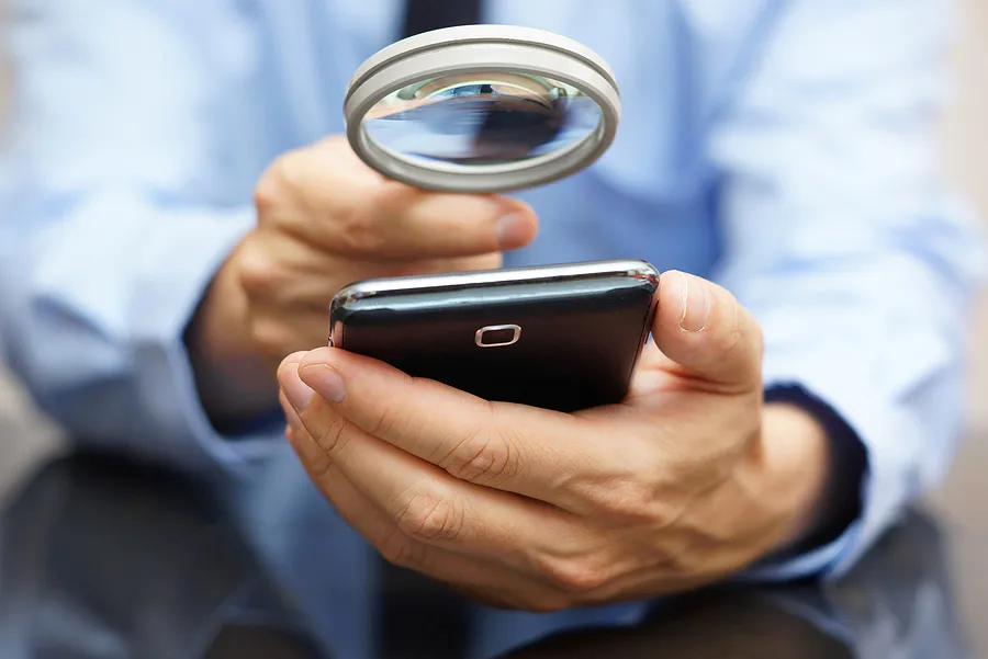 Eine Person, die ein Smartphone mit einer Lupe genau unter die Lupe nimmt, um das Gerät auf Echtheit oder Mängel zu überprüfen.
