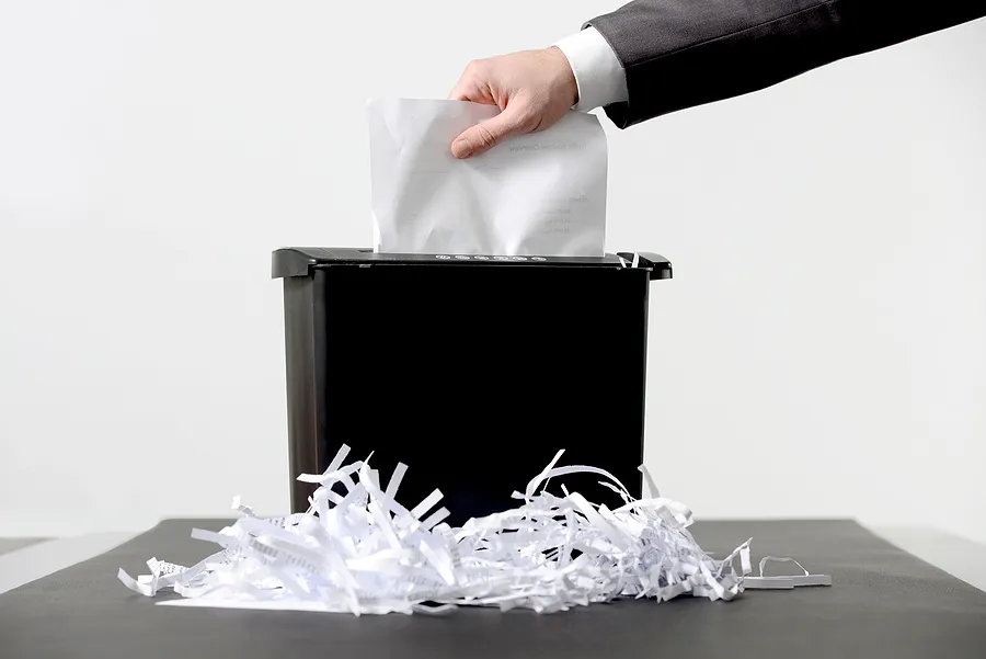 Dokumente werden von Hand in einen Aktenvernichter eingelegt, um die zertifizierte Datenvernichtung und die sichere Entsorgung sensibler Informationen zu veranschaulichen.
