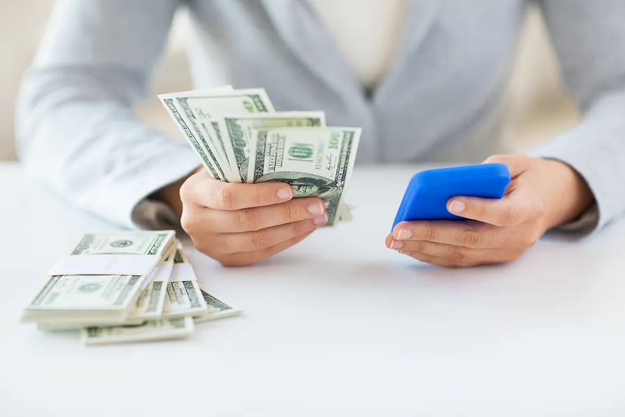 Eine Person, die in der einen Hand ein Smartphone und in der anderen Bargeld hält, was den Wiederverkaufswert des Handys symbolisiert und den Verkauf eines gebrauchten Handys gegen Bargeld darstellt.